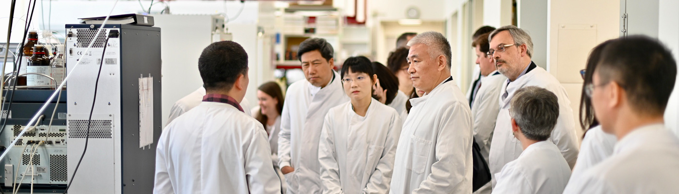 A group of people in white lab coats tour a scientific facility